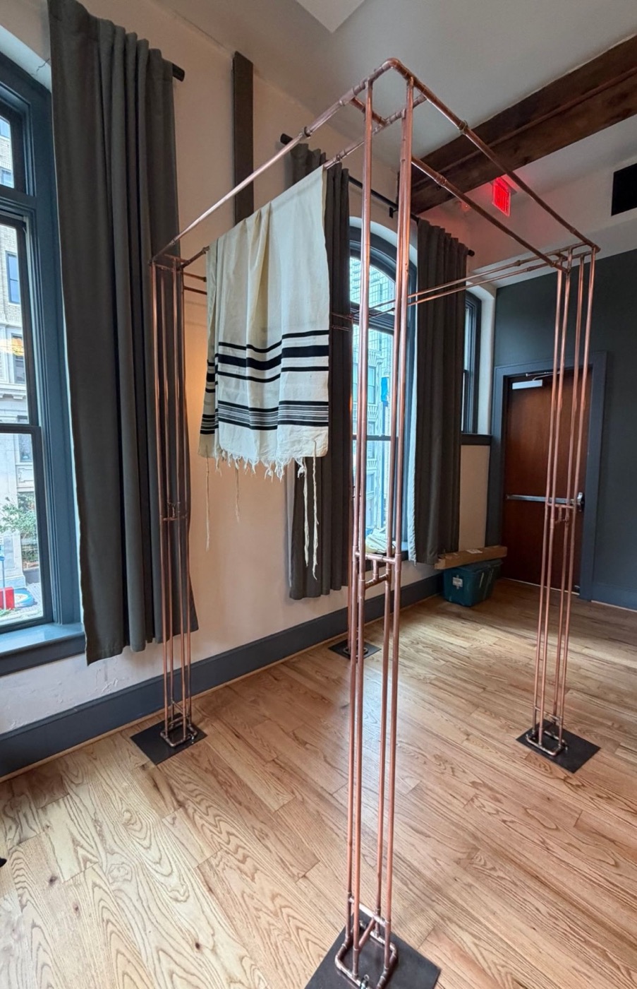 The bare copper chuppah frame on steel base plates with a tallit draped across the top
