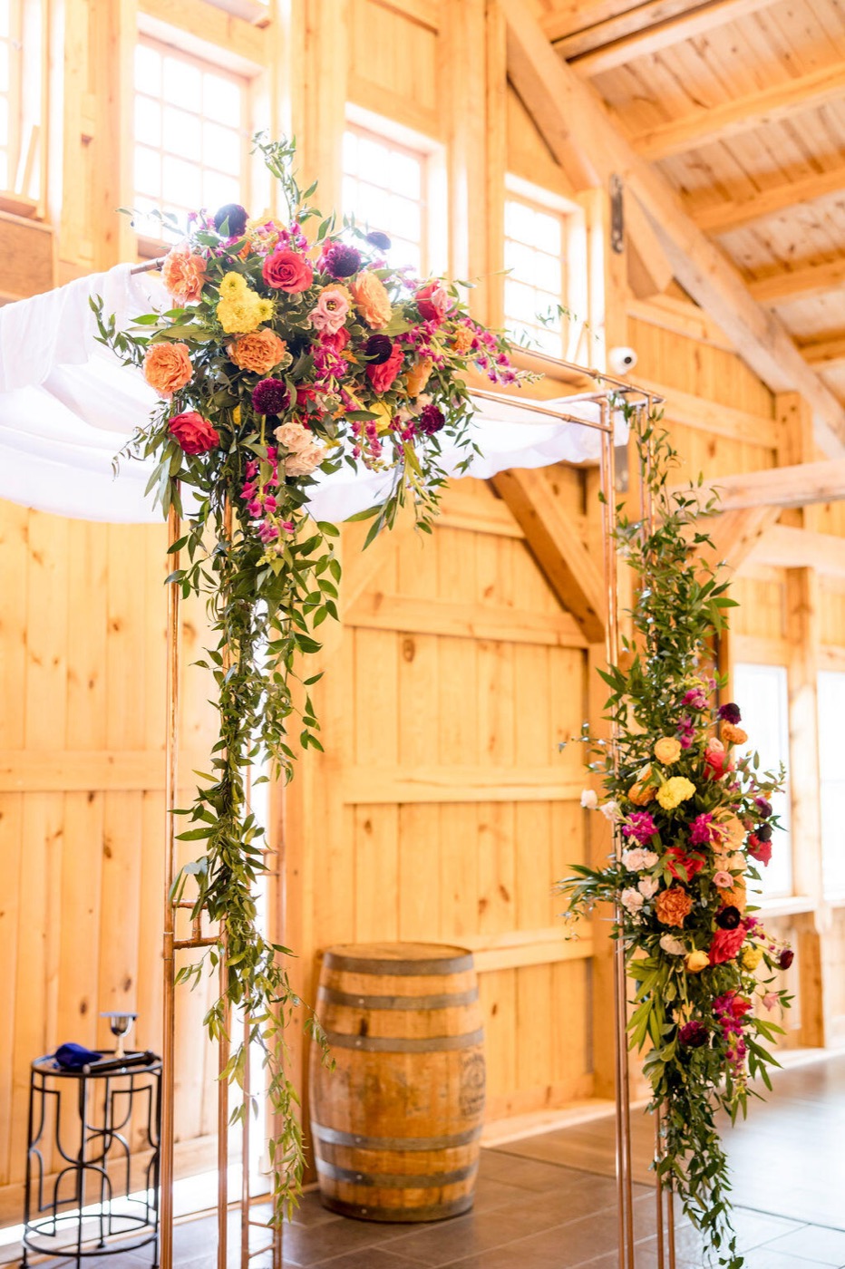 Copper chuppah with a white canopy and bright florals inside a timber barn