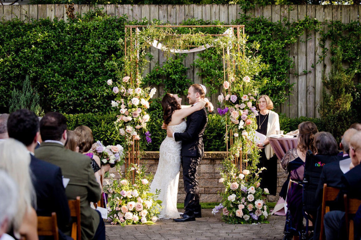 A couple embracing under the copper chuppah during their ceremony
