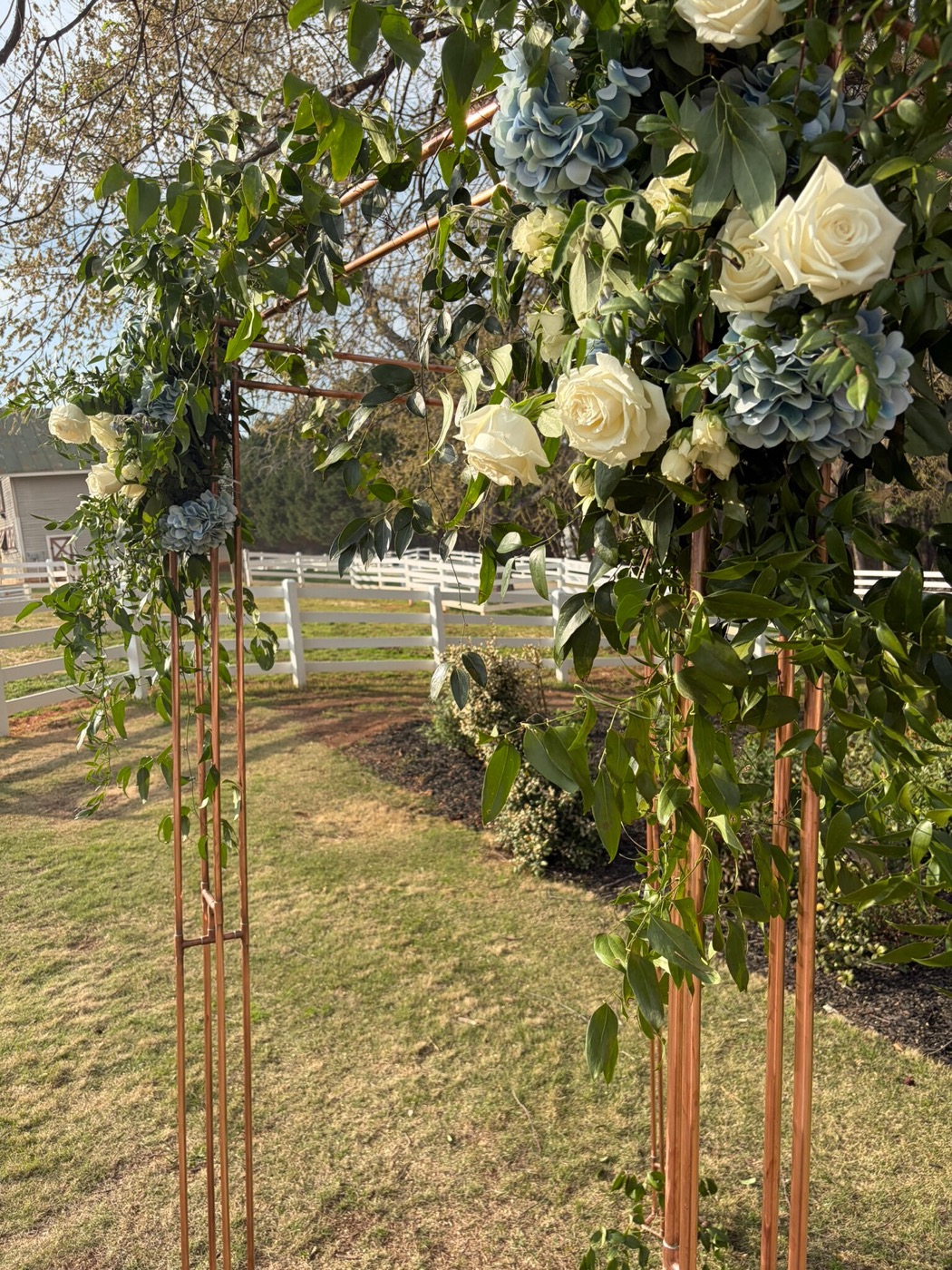Copper chuppah with white roses and blue hydrangeas on a lawn